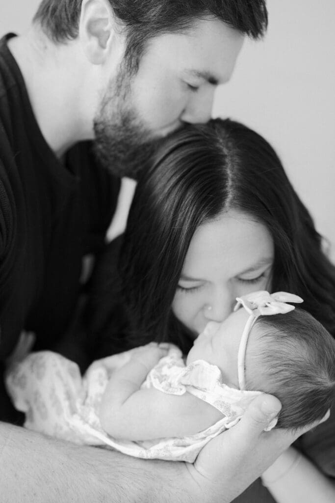 Parents holding their newborn baby during a cozy in home newborn photography session in Hampton Roads with soft natural window light and neutral tones.
