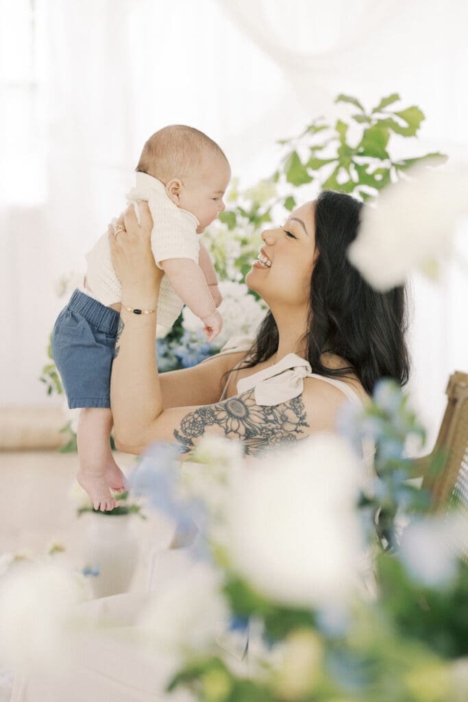 Mother holding her baby boy in a soft floral Mother’s Day studio setup filled with natural light and airy spring blooms in Hampton Roads Virginia.