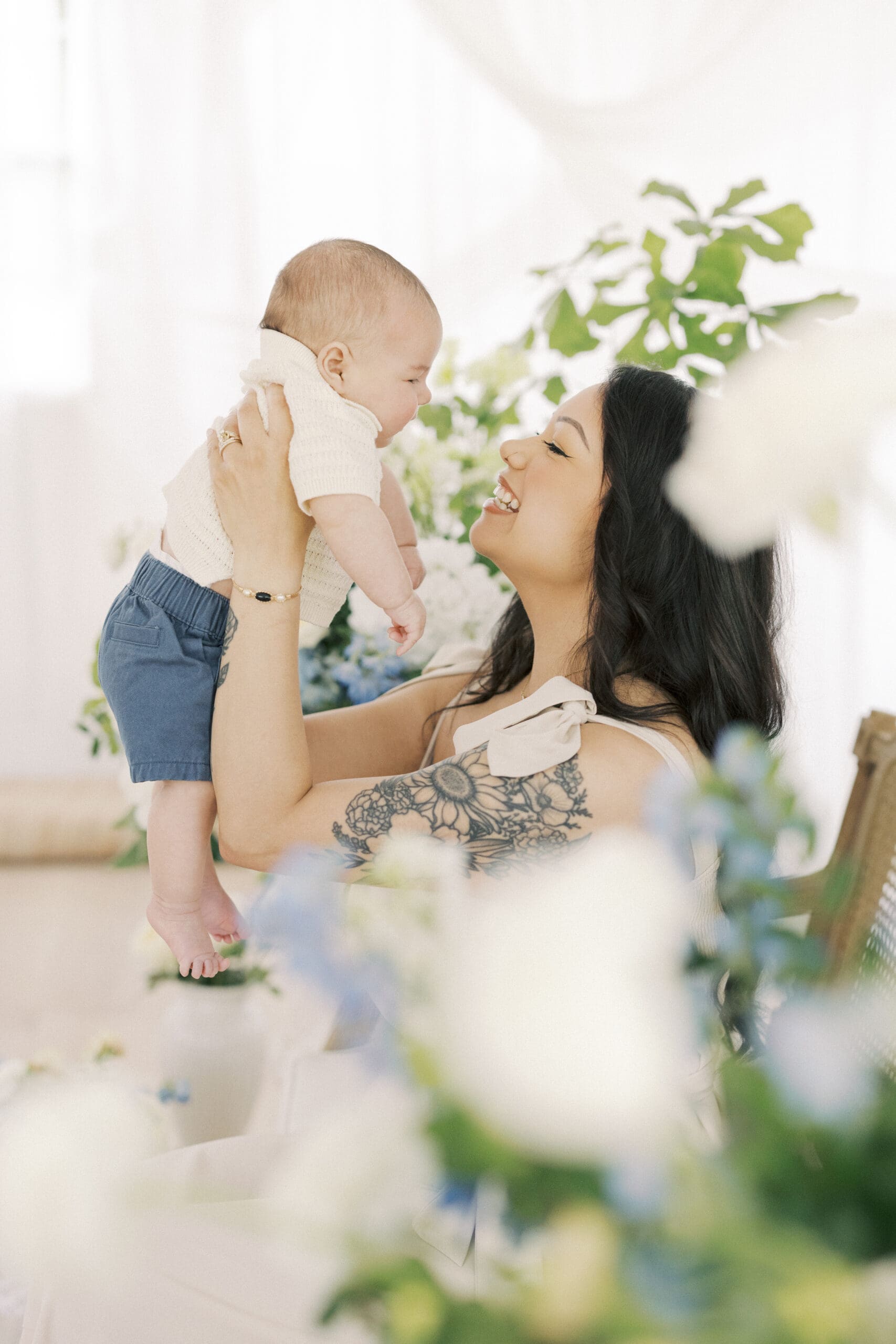 Mother holding her baby boy in a soft floral Mother’s Day studio setup filled with natural light and airy spring blooms in Hampton Roads Virginia.